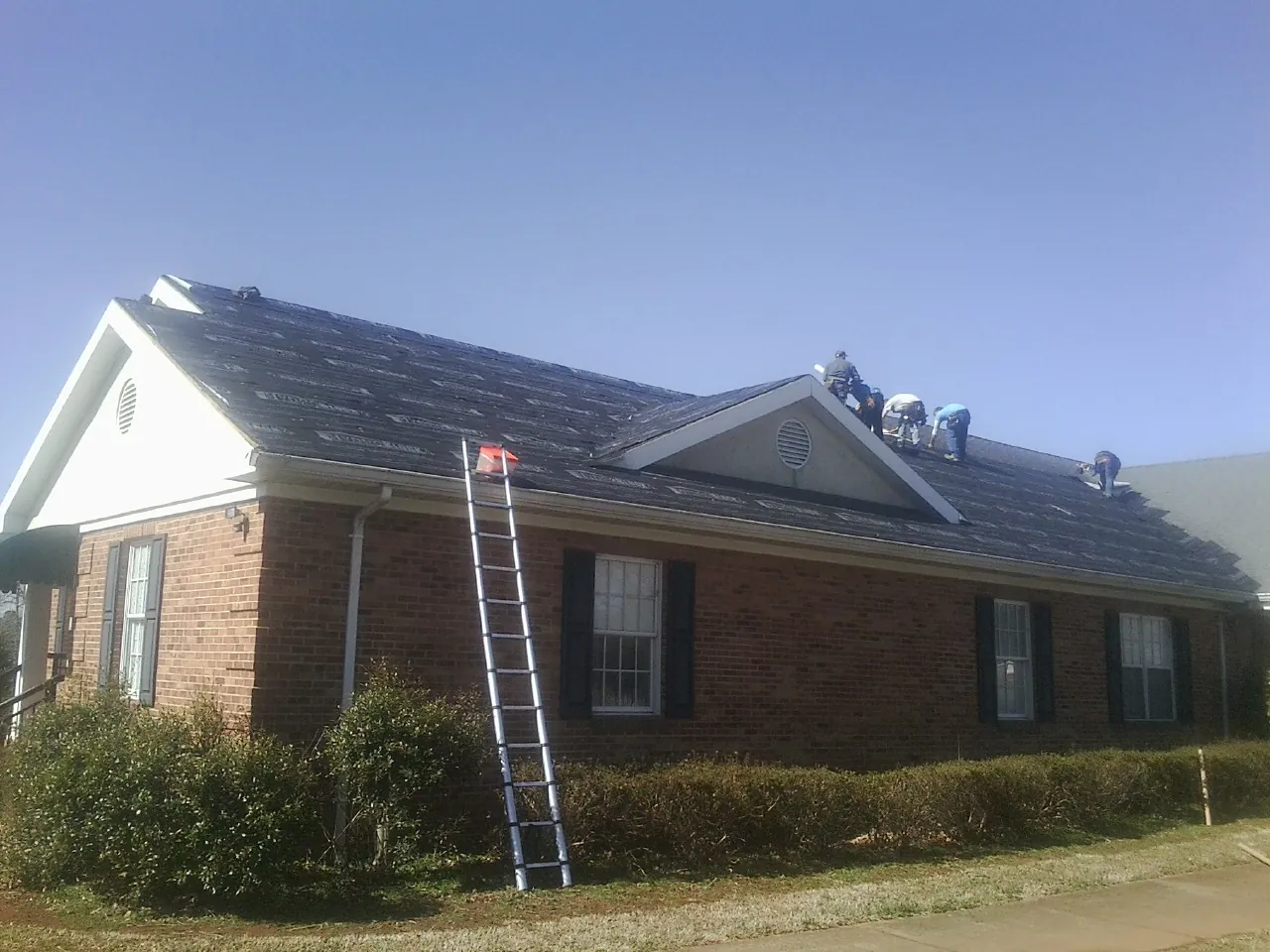 Crew tearing shingles off a brick ranch roof with a ladder set — Emergency Roof Repair work by our crew in Sherrill