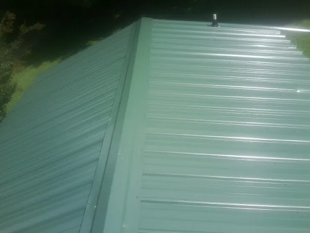 New green metal panels meeting at the ridge of a roof — Flat Roof Repair work by our crew in Sherrill
