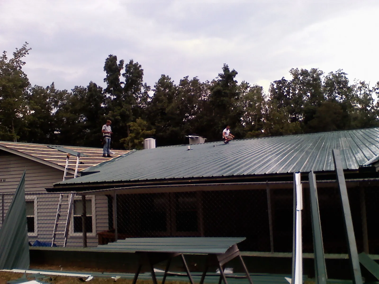 Two roofers installing green metal panels above a covered porch in Sherrill