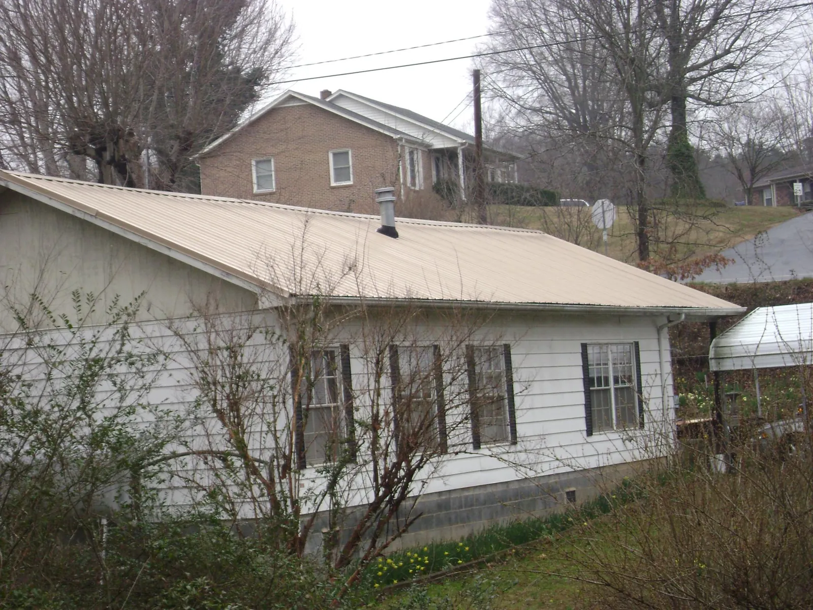 Tan metal roof on a white sided house set into a hillside — Commercial Roofing by Roofing Brothers in Sherrill